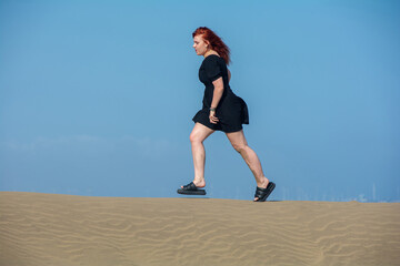 Young woman running on a sand dune, with blue sky