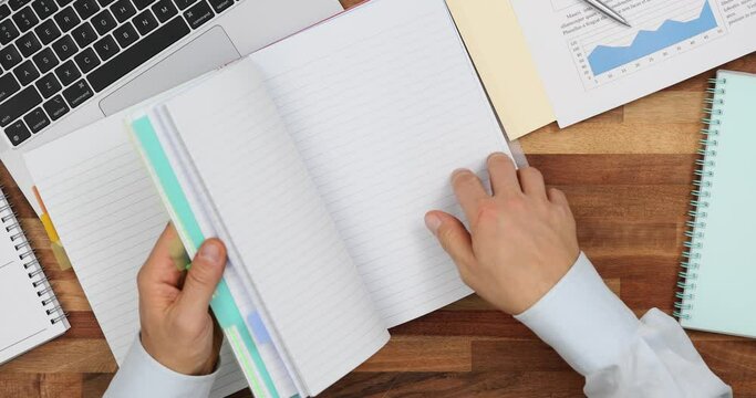 Man hand flips through blank colored notebook at workplace top view