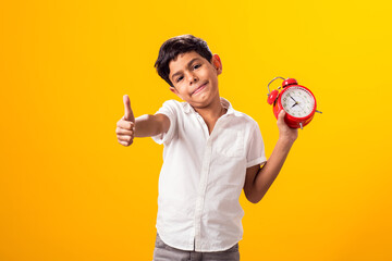 Kid boy holding alarm clock and showing thumb up gesture. Education and time management concept - obrazy, fototapety, plakaty
