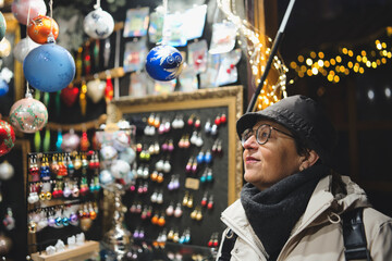 Old woman shopping at the Christmas street market, choosing gifts. Winter holidays, travel,...