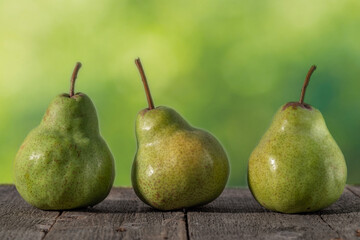 Three green pears on a wooden table with a blurred green background