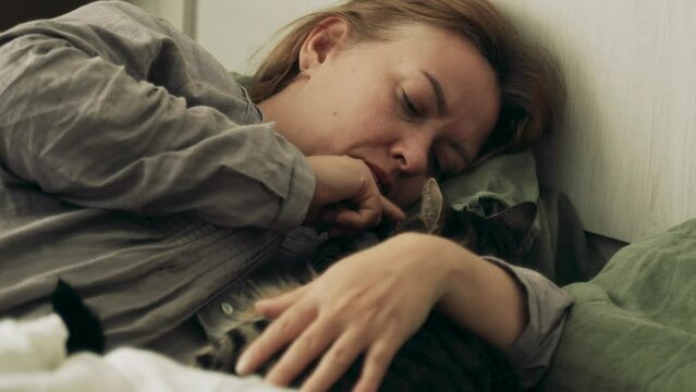 A woman lies with a cat, stroking its paws. Love for cats.
