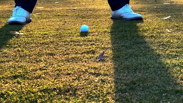 Low Angle View on a Male Golfer Hitting with His Golf Club Iron the Ball on the Fairway in Sunset on the Golf Course with Shadow on the Grass in Switzerland. (Slow Motion)