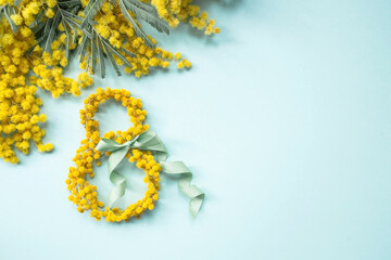 International Women's Day. A banner, a flyer, a beautiful postcard for March 8th. Yellow mimosa flowers in the shape of the number eight and a ribbon bow on a turquoise, blue background. - obrazy, fototapety, plakaty