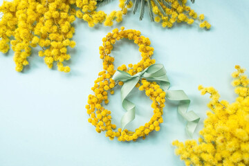 International Women's Day. A banner, a flyer, a beautiful postcard for March 8th. Yellow mimosa flowers in the shape of the number eight and a ribbon bow on a turquoise, blue background.