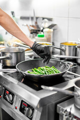 Professional chef cooking asparagus in frying pan on stove in restaurant kitchen