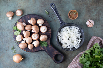 Champignons lie on cutting board next to a frying pan filled with chopped onions