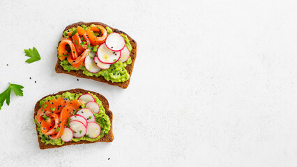 Healthy breakfast toasts with avocado, salmon, radish, and herbs on a white background. Copy space.