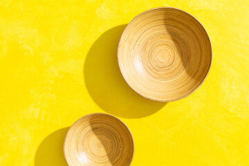Two empty bamboo bowls on a bright yellow background.