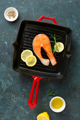Raw salmon steak in a cast-iron grill pan with lemon and rosemary.