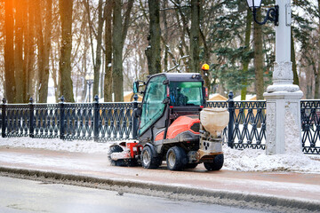 Tractor with rotating brush sweep snow from sidewalk. Small tractor clear snow from footpath, snow...