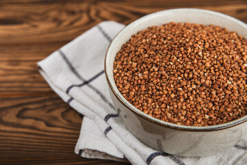 Raw buckwheat in a bowl on a textured wooden background. Wheat grains, porridge, cereals, raw buckwheat in a plate. Healthy food. Porridge. Diet. Organic cerea. Space for text.Copy space.