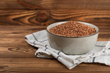 Raw buckwheat in a bowl on a textured wooden background. Wheat grains, porridge, cereals, raw buckwheat in a plate. Healthy food. Porridge. Diet. Organic cerea. Space for text.Copy space.