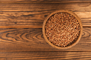 Raw buckwheat in a bowl on a textured wooden background. Wheat grains, porridge, cereals, raw buckwheat in a plate. Healthy food. Porridge. Diet. Organic cerea. Space for text.Copy space.