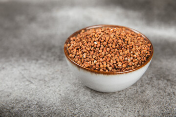 Raw buckwheat in a bowl on a textured wooden background. Wheat grains, porridge, cereals, raw buckwheat in a plate. Healthy food. Porridge. Diet. Organic cerea. Space for text.Copy space.