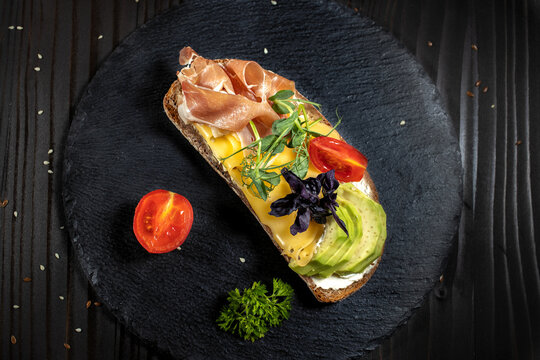 Tasty open sandwich with ham,avocado, cheese and cherry tomato on a black background
