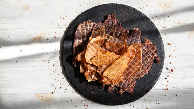 Dried meat pieces on black plate.Jerky slices.