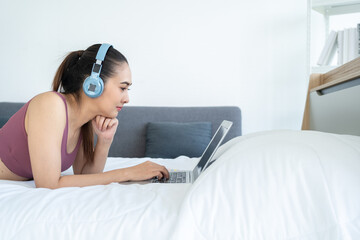 Happy Young beautiful asian fitness woman relax after work out on the bed. Cheerfully sporty female using laptop.