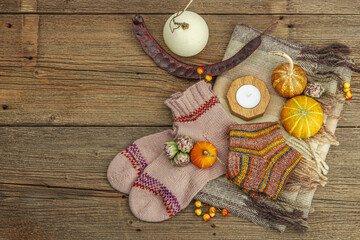 Autumn cozy composition. Scarf, warm knitted socks, candle, pumpkins, fall decor. Wooden background