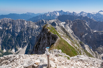 Panorama on top of untamed mountain peak mount Mangart (Mangrt), border Italy Slovenia. Scenic view of majestic mountain peaks of Julian Alps, blue sky summer day. Climb rugged extreme alpine terrain