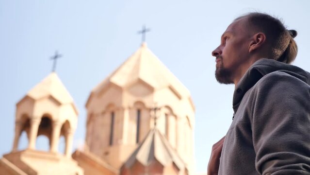 Side view, a handsome young man with a fashionable hairstyle crossed himself in a Christian manner, looking at the Christian temple and bowed. gesture of crossing one's fingers. Religion Concept