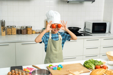 Asian Little chef boy cooking breakfast in the kitchen. Funny kids are preparing food with ingredient. Cute little asian boy a in chef with chef uniform