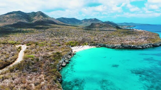 The drone is flying above the ocean looking at a small beach and the mountains in the background in Curacao Aerial Footage 4K