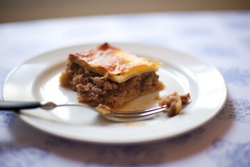 half-eaten slice of moussaka on a white plate with a fork