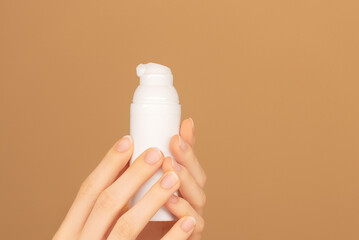 Female palms holding white bottle jar with face moisturizing cream dispenser on isolated peach background. Ready template for brand presentation. Skin care ad, copy space. 