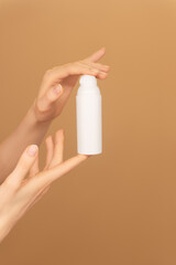 Female palms holding white bottle jar with face moisturizing cream dispenser on isolated peach background. Ready template for brand presentation. Skin care ad, copy space. Vertical photo