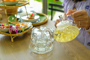 Woman is pouring jasmine tea from glass kettle into a cup