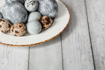 Stylish grey Easter eggs in the color of marble, concrete in a plate and willow branches on a white wooden background. Coloring eggs with natural dye karkade tea. Easter 2024. 