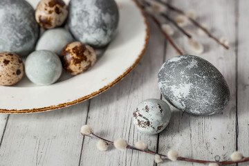 Stylish grey Easter eggs in the color of marble, concrete in a plate and willow branches on a white wooden background. Coloring eggs with natural dye karkade tea.  The feast of bright Easter.