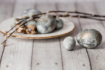 Stylish grey Easter eggs in the color of marble, concrete in a plate and willow branches on a white wooden background. Coloring eggs with natural dye karkade tea. The feast of bright Easter.