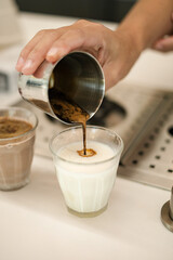 Someone’s hand is pouring coffee into milk glass