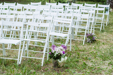 White wooden chairs placed in rows on a lawn. Place for wedding ceremony or other events in botanic garden. Seats for visitors. Wedding Florals for a spring wedding ceremony with rows of white chairs - 706327750