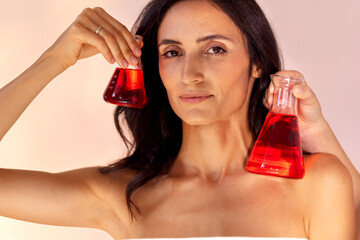 Close-up of female studio portrait of gorgeous young woman with glass flasks with red liquid....