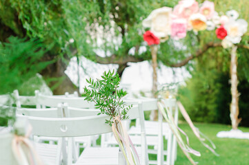 White chairs decorated with pistachio branches against the backdrop of a wedding arch.