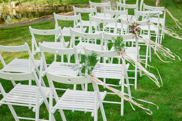 White Folding Chairs Adorned with Ribbons, Pistachio Branches and Other Plants at a Wedding Ceremony