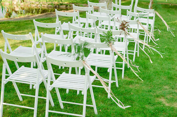 White Chairs Adorned with a Garland of Pistachio and Other Plants at a Wedding Ceremony