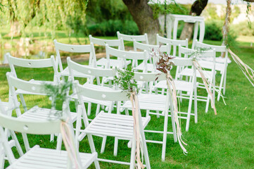 Natural Elegance: White Folding Chairs Embellished with Ribbons, Pistachio Branches, and Greenery at a Wedding Ceremony - 706330980