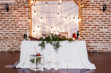 Bride and Groom's Wedding Table against the Brick Wall and Hanging Bulbs on the Wedding Arch. - 706331195