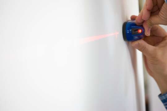 Man's Hands Holding Laser Level against White Wall
