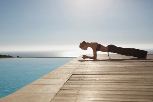 Young woman practicing yoga by a swimming pool with ocean in the background

