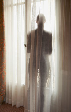 Silhouette of a woman behind a semi transparent curtain, back view
