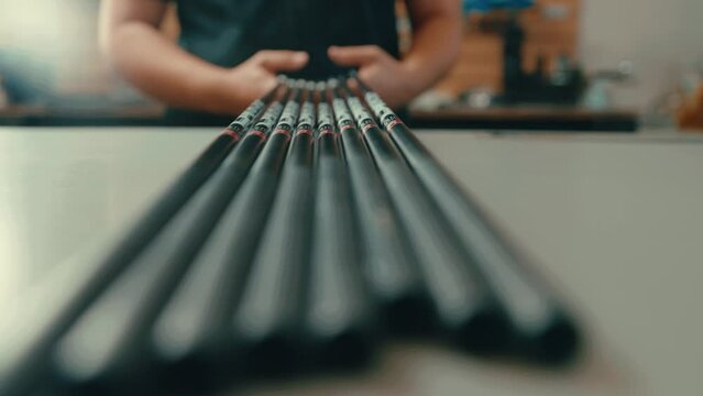 Male hands grab set of golf club shafts off counter top in workshop in slow motion