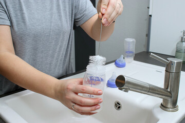 Close up of mothers hands cleaning a baby milk bottle with a brush, home kitchen sink