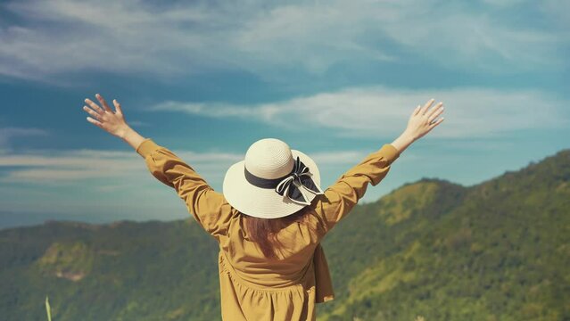 Young asian female tourist raised hands into breathing the fresh air looking at beautiful mountain view. Woman traveler stands alone with open arms in mountains. Natural beauty. Travel concept