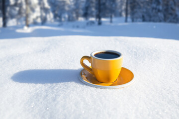 Winter background. Yellow cup with hot coffee or tea stand on the snow outdoor at sunny day with...