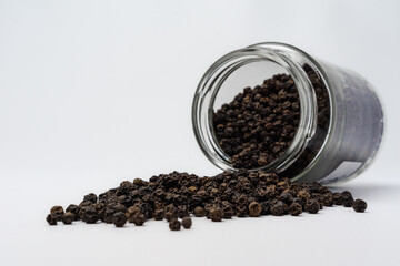 black peppercorn spill out from it's jar, isolated on a white background, concept of spice catalog